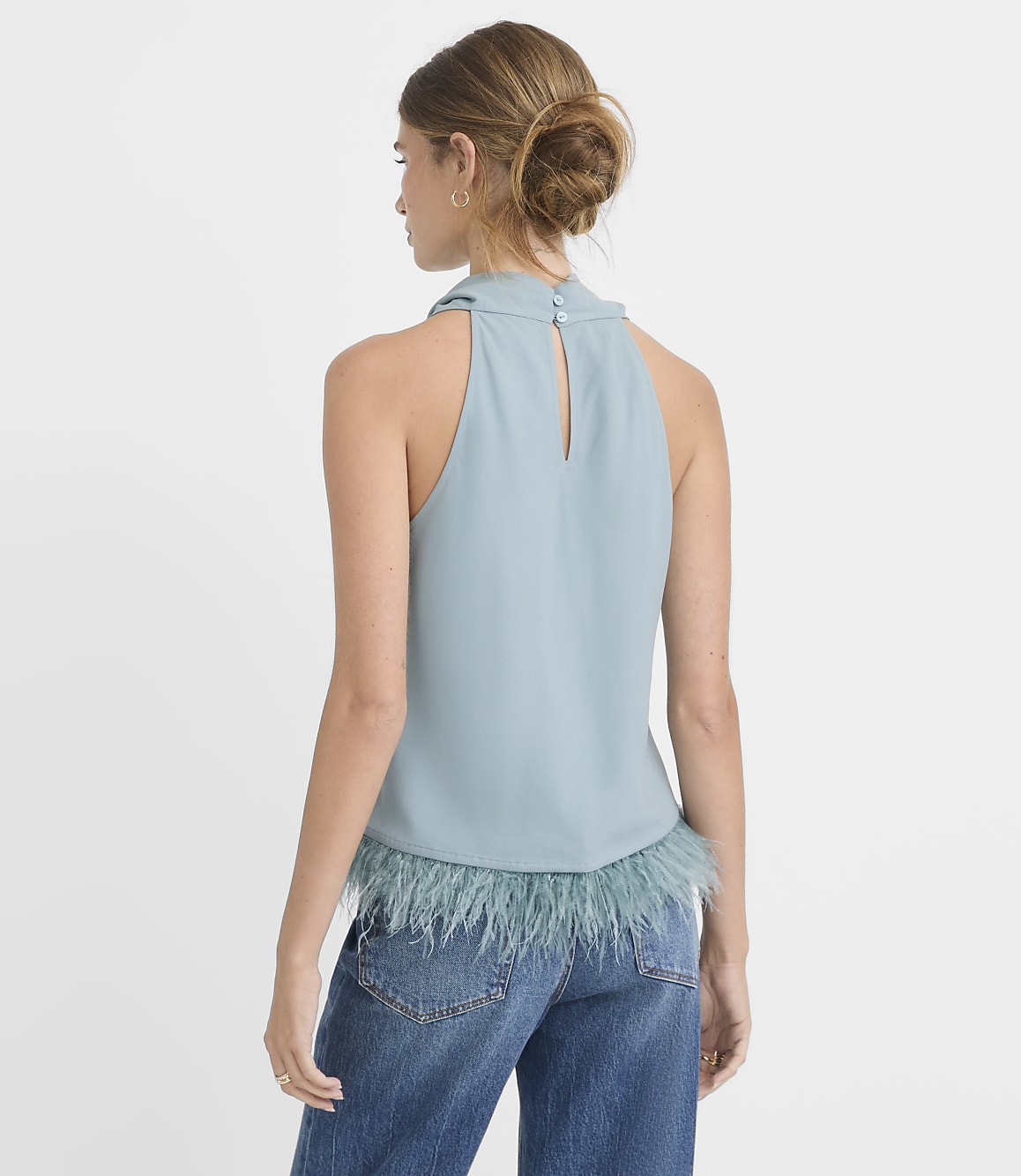 A woman in a blue halter top with feather trim stands against a plain white background.