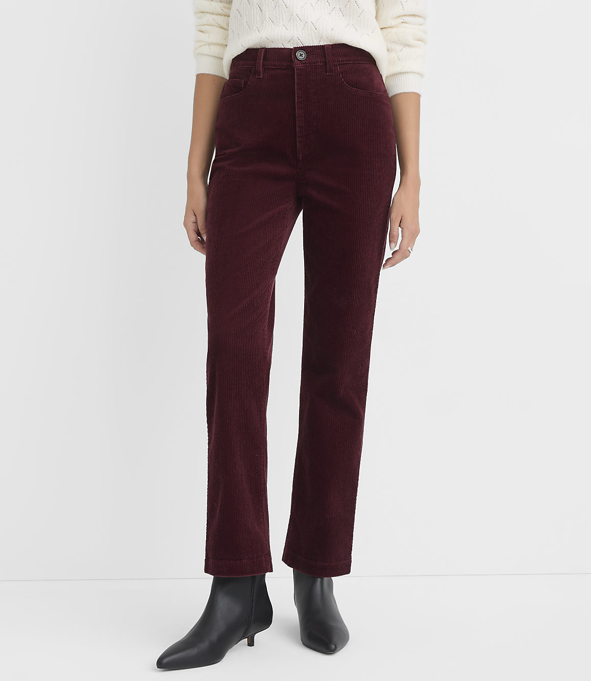 A person stands in burgundy corduroy pants and black boots against a plain white background.