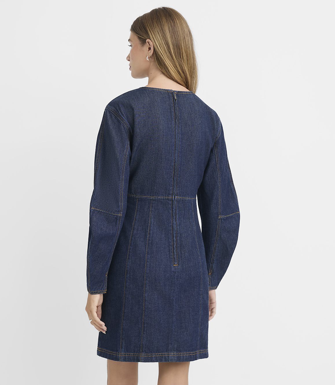 A woman in a dark denim dress stands against a plain white background.