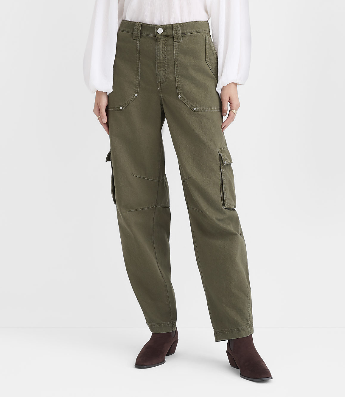 A person wearing a white blouse, olive green cargo pants, and dark brown ankle boots stands against a plain white background.