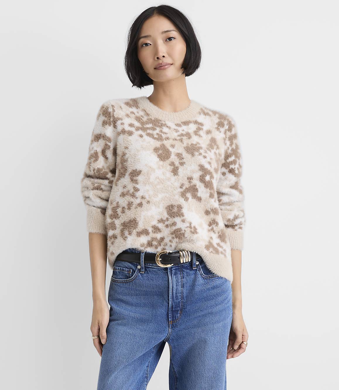 A woman wearing a leopard-print fuzzy sweater and blue jeans stands against a plain white background.
