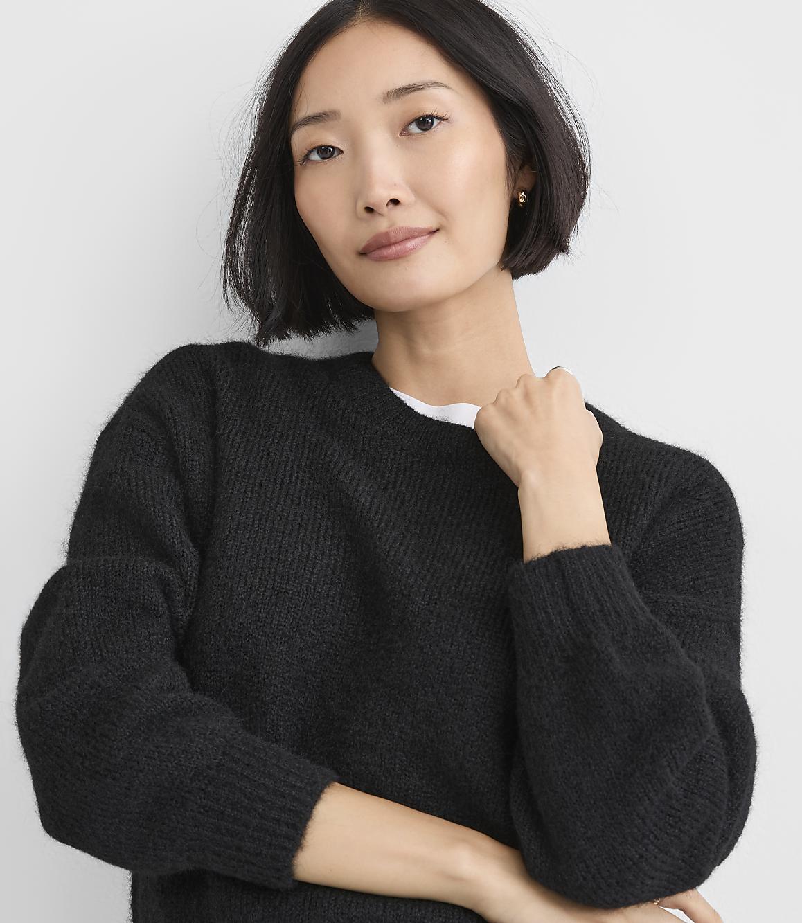 A woman with short dark hair wearing a black knit sweater poses against a plain white background.