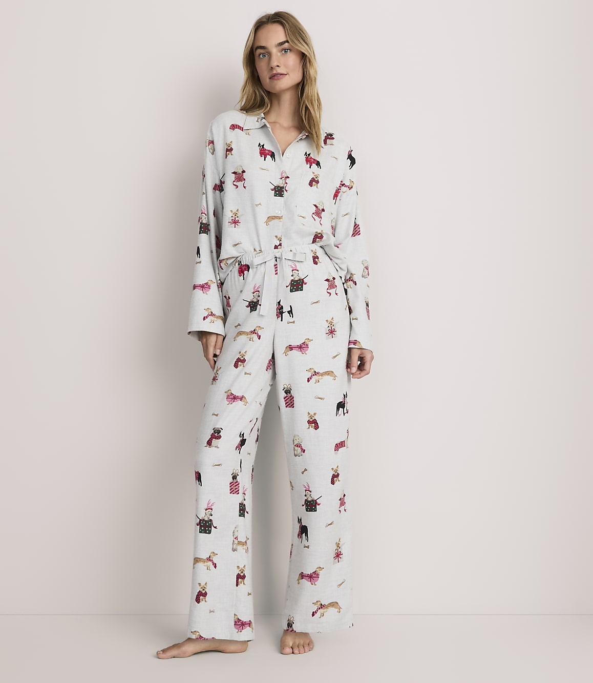 A woman stands wearing light blue dog-patterned pajamas against a plain, neutral background.