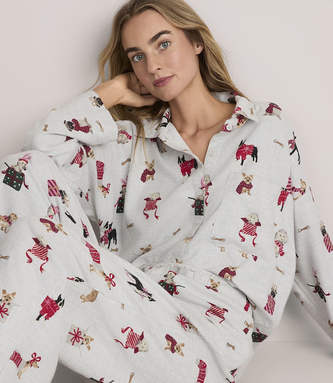 A woman wearing light grey pajamas with a red and black dog print poses against a plain white background.