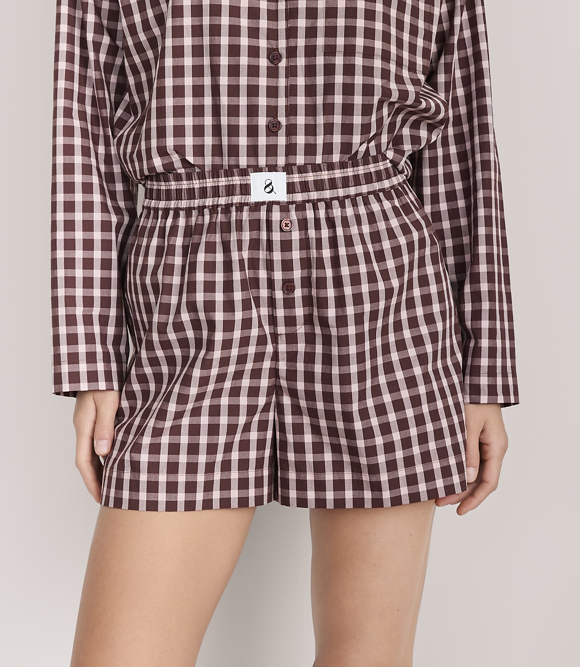 A person wears a matching maroon and white gingham pajama set against a plain light gray background.