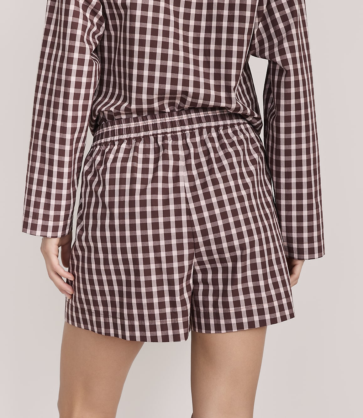 A person wearing a brown and white checkered pajama set stands against a plain, light-colored background.