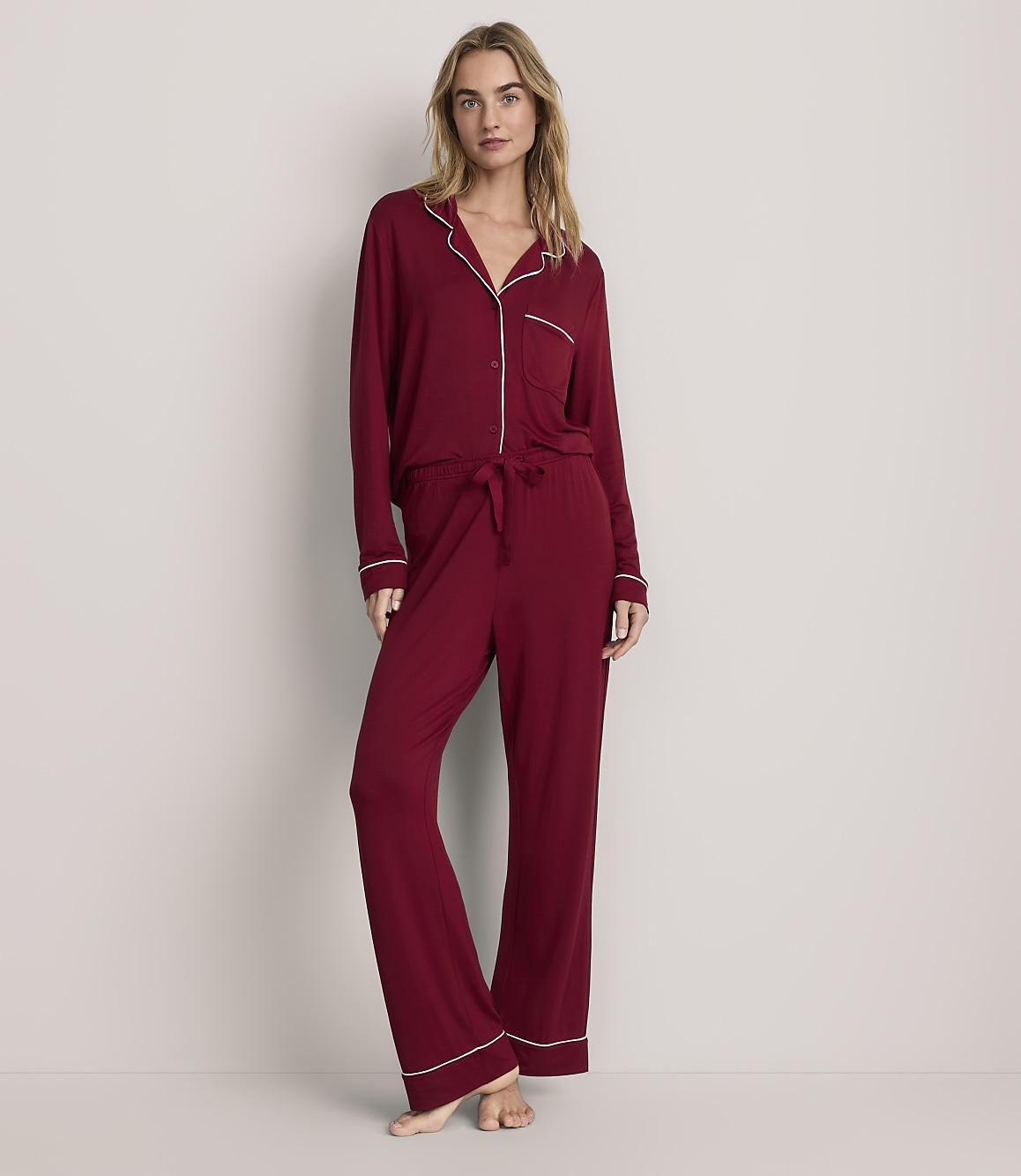 A woman wearing red pajamas with white trim stands against a plain, light-colored background.