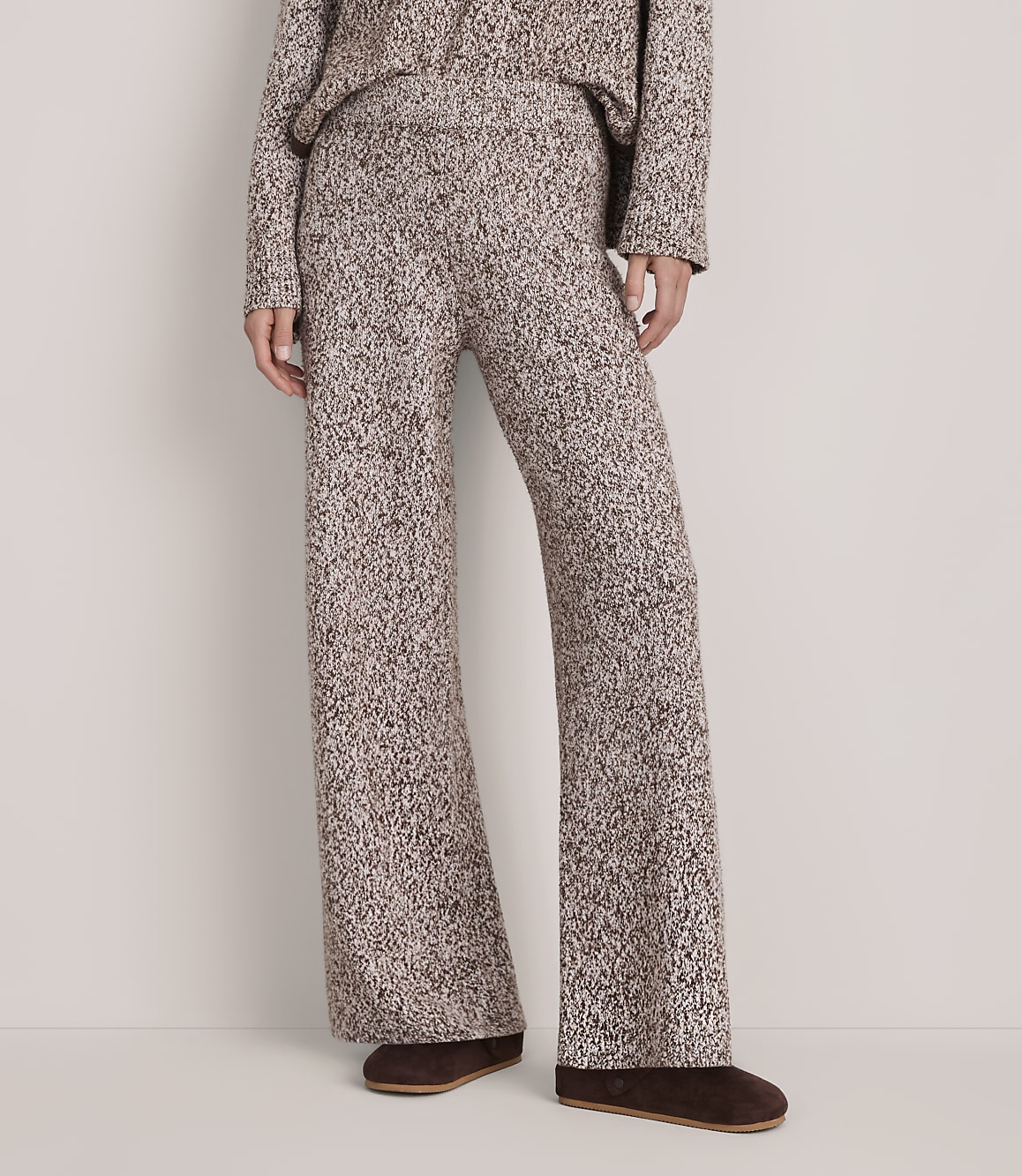 A person wears a matching brown and white textured knit set with brown loafers against a plain white background.