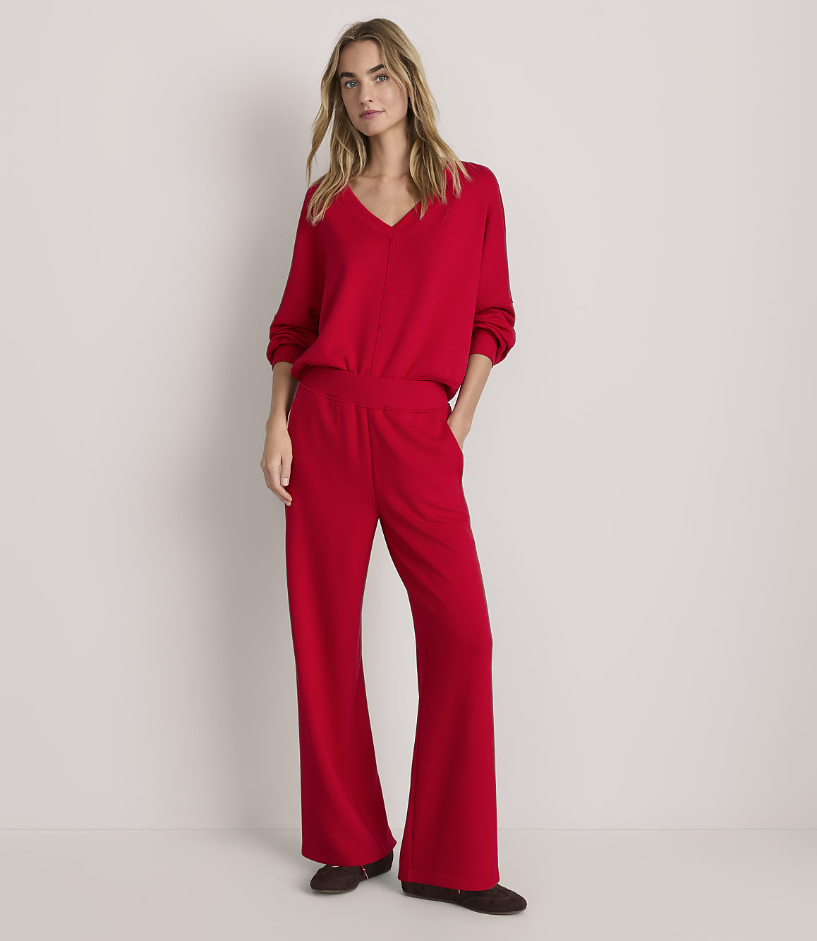 A woman wearing a red V-neck sweater and matching wide-leg trousers stands against a plain, light-colored background.
