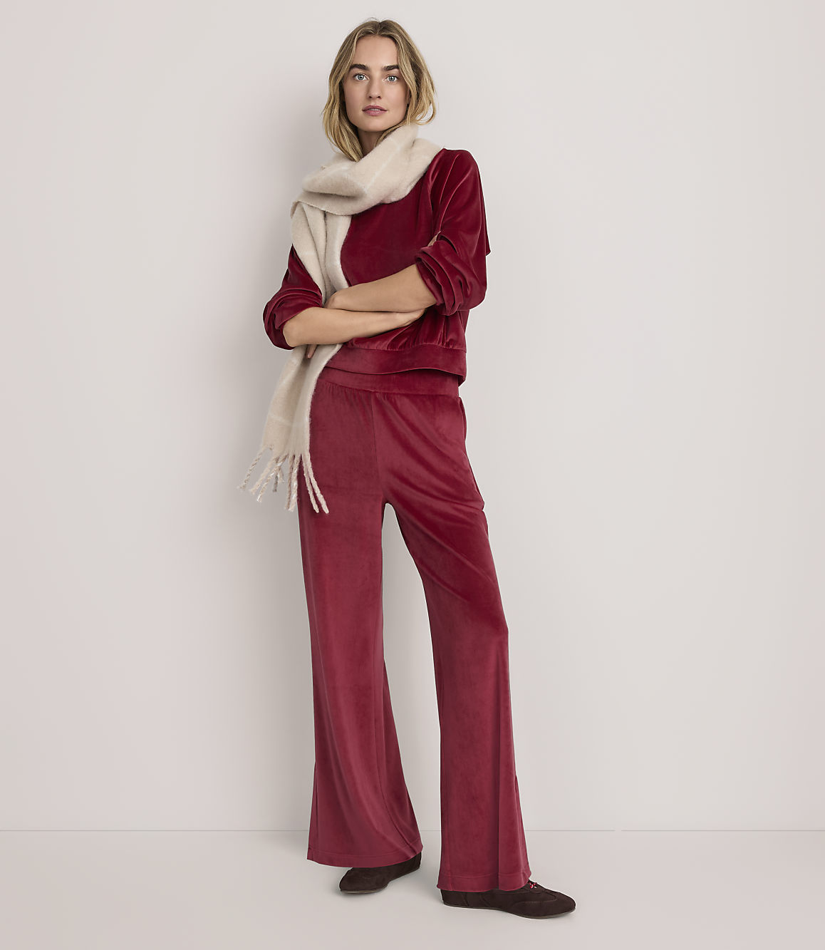 A woman wearing a red velvet two-piece outfit and a cream scarf stands against a plain white background.