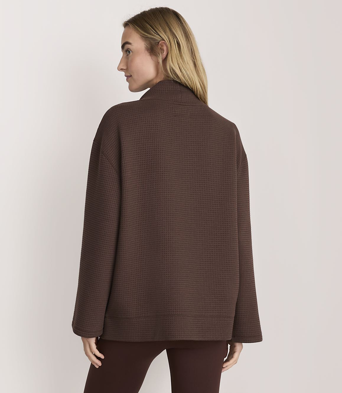 A woman wearing a brown textured jacket and matching leggings stands against a plain white background.