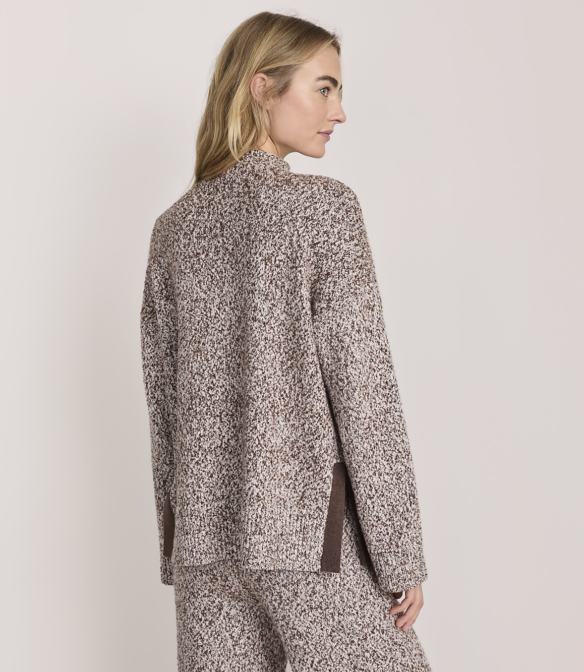 A woman wearing a brown and white speckled knit set stands against a plain, light-colored background.