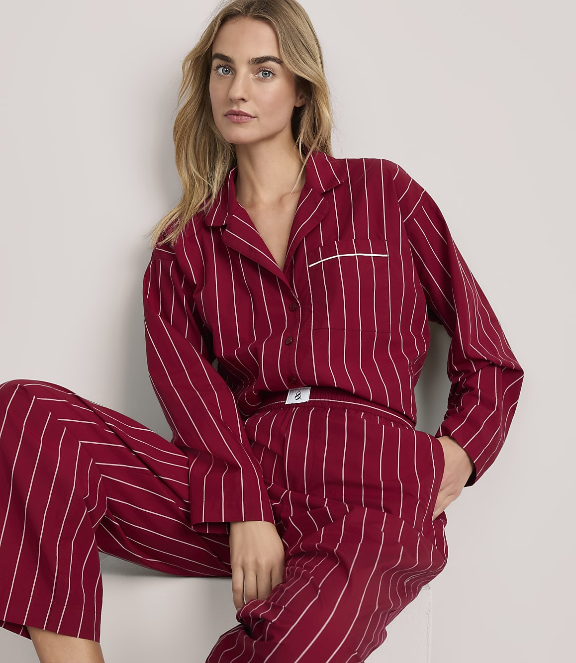 A blonde woman wearing red and white striped pajamas poses against a plain white background.