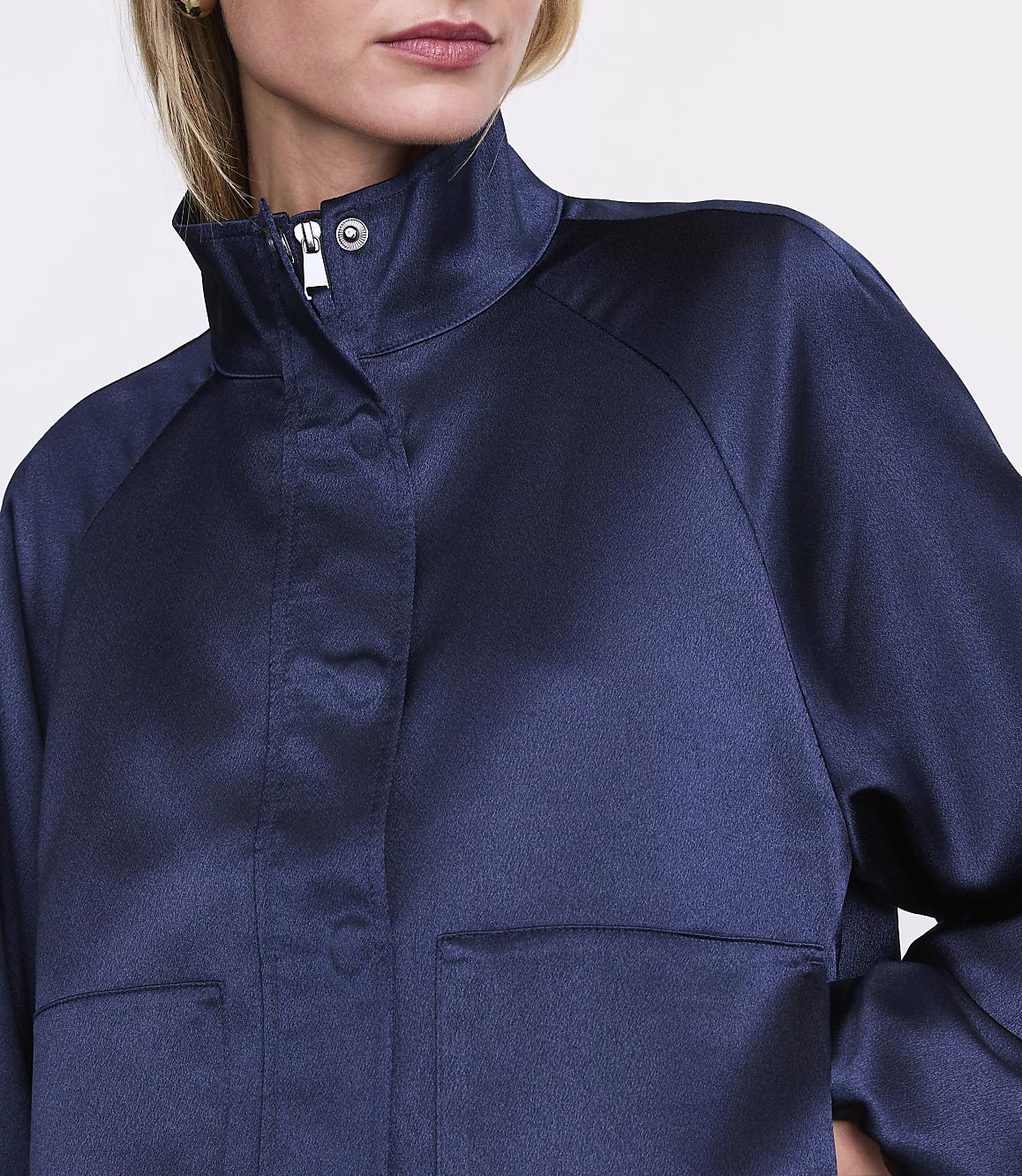 A person wearing a navy blue satin jacket stands against a plain white background.