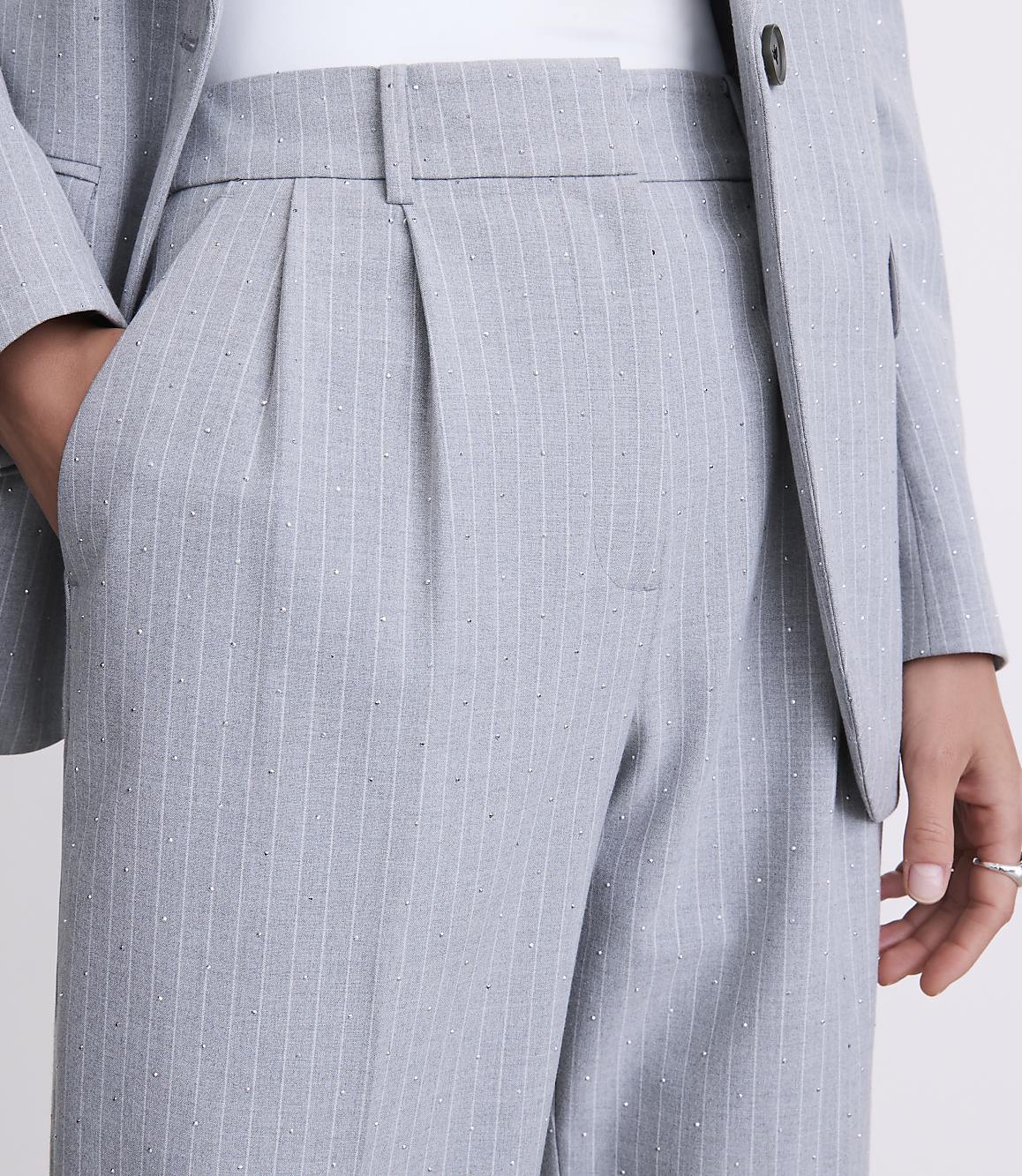 A person wears a grey pinstriped suit with shimmering accents against a plain white background.