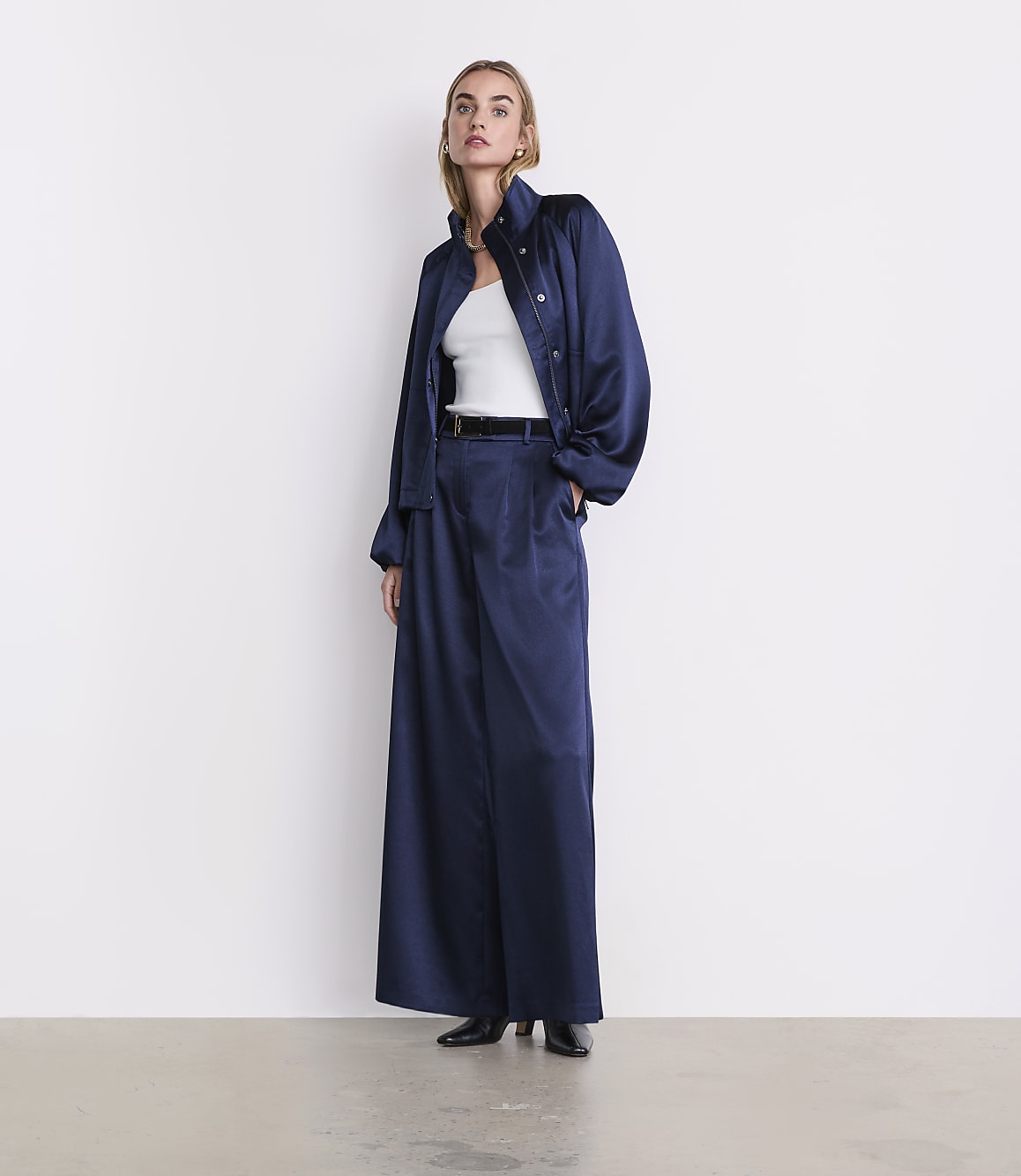 A woman wearing a navy blue satin suit over a white top stands against a plain white background.