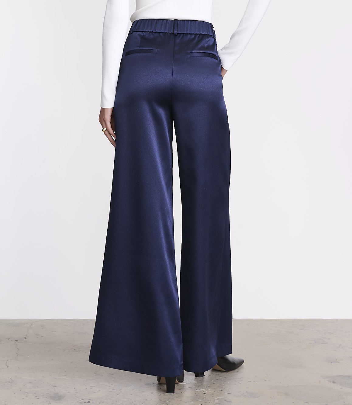 A person wearing a white long-sleeved top and wide-leg navy blue satin trousers stands against a plain white background.