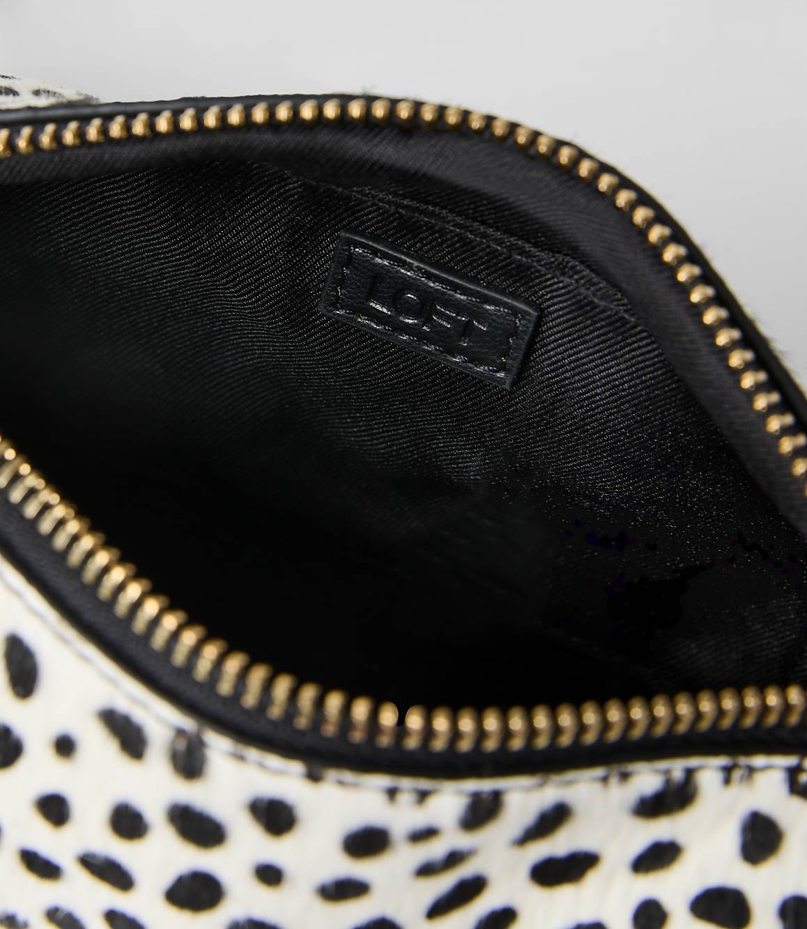 A white and black spotted pouch with a gold zipper and black interior is set against a plain light gray background.