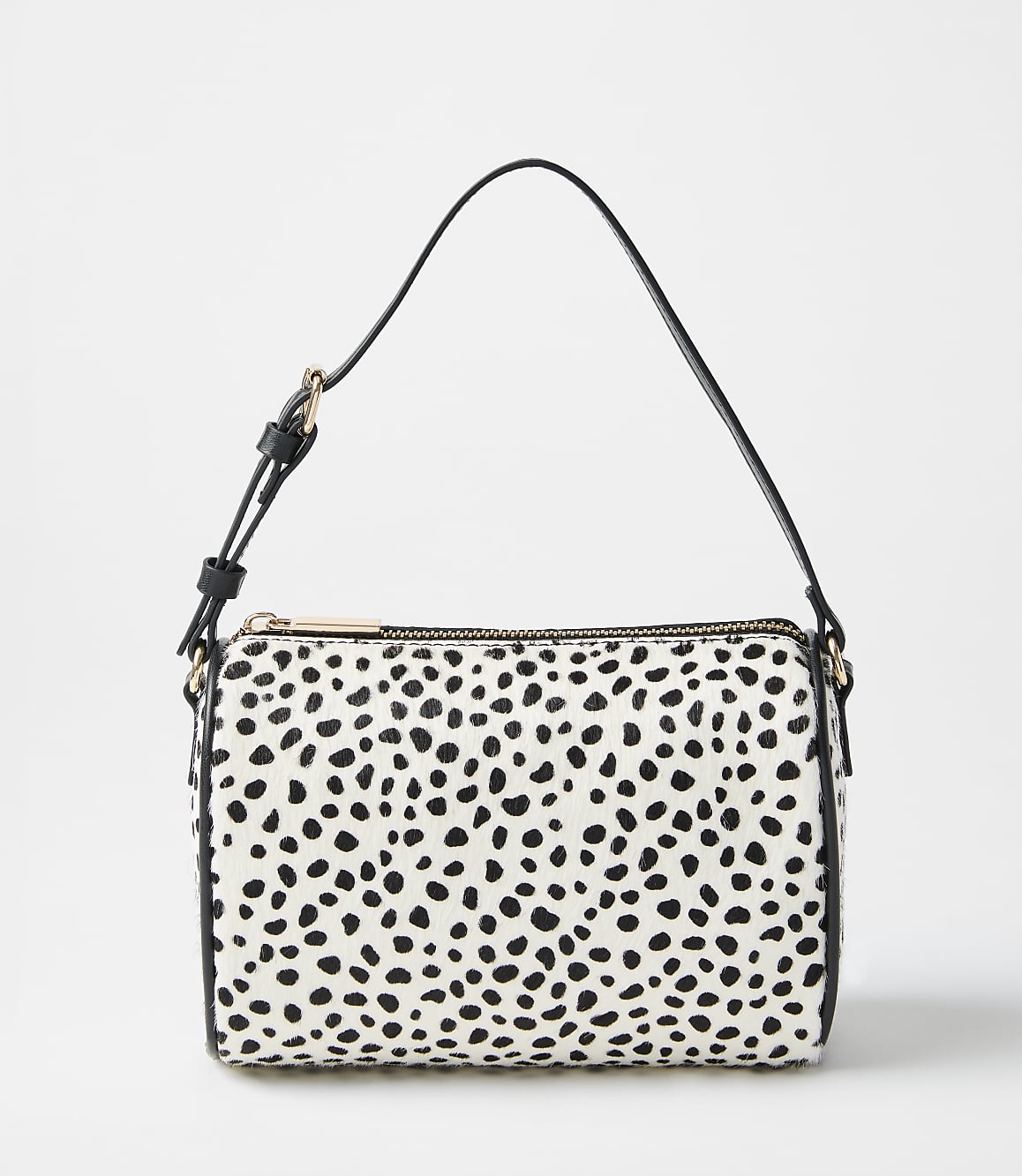 A white and black spotted handbag with a black strap sits against a plain, light gray background.