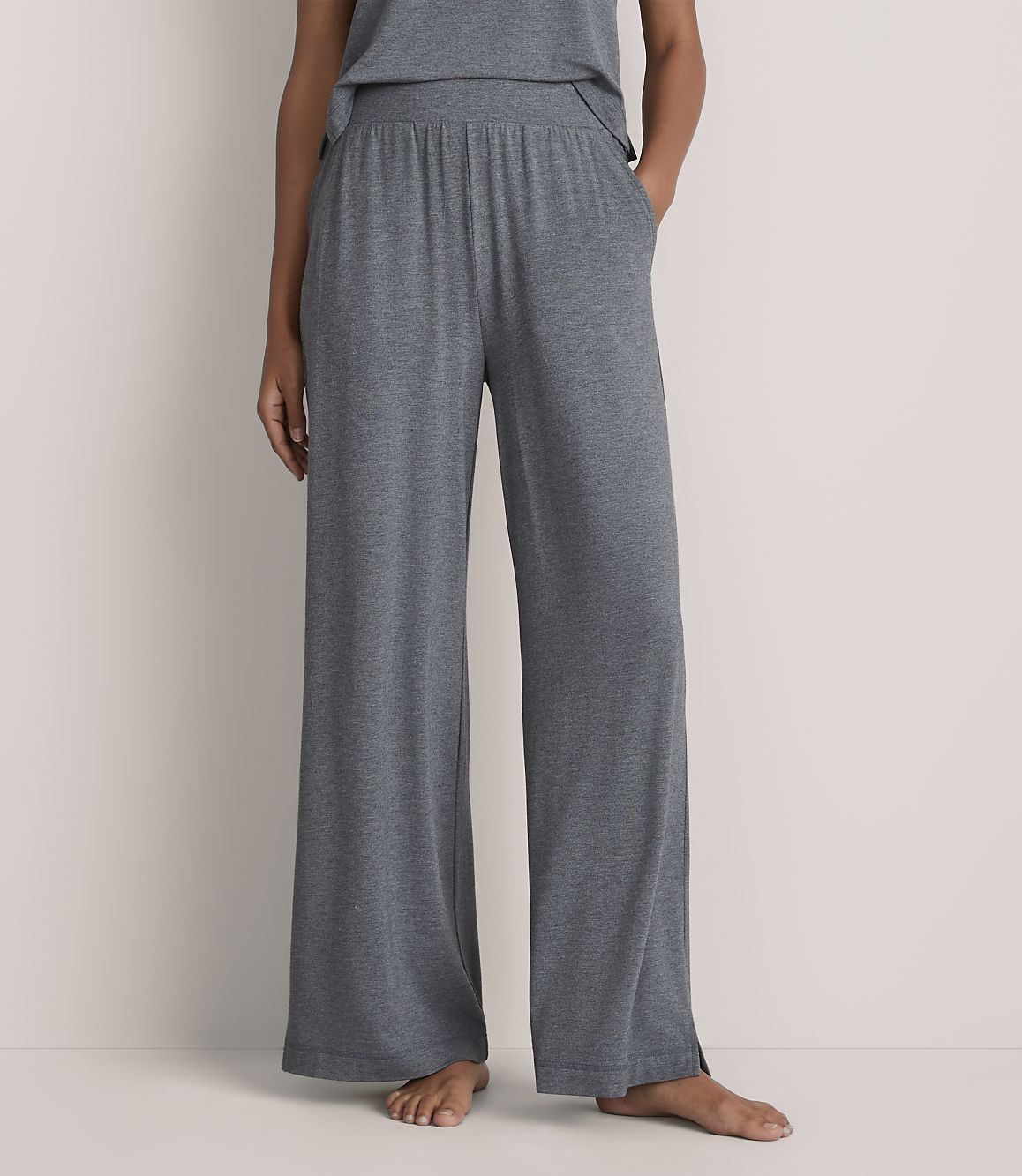 A person wearing wide-leg grey lounge pants stands against a plain, light-colored wall.