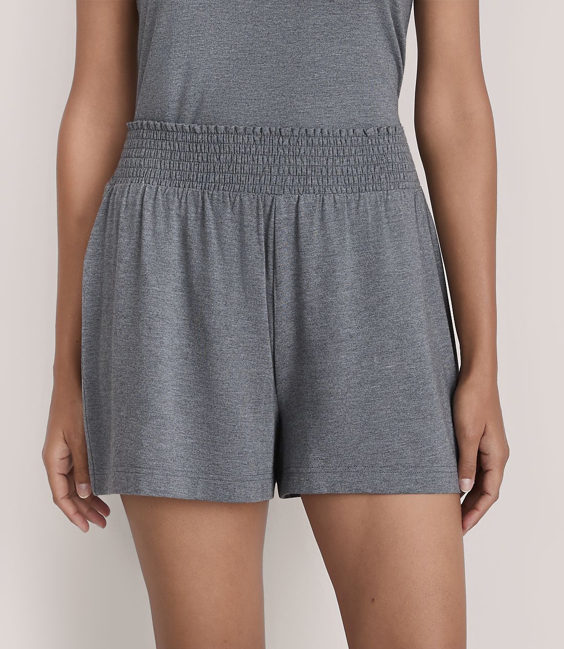 A person wears grey elastic-waist shorts against a plain, light-colored background.
