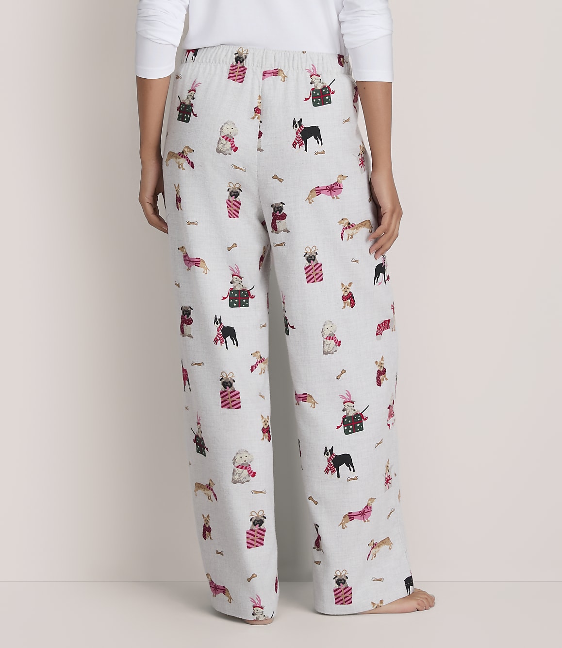 A person wears white pajama pants featuring a festive dog print against a plain, light-colored background.