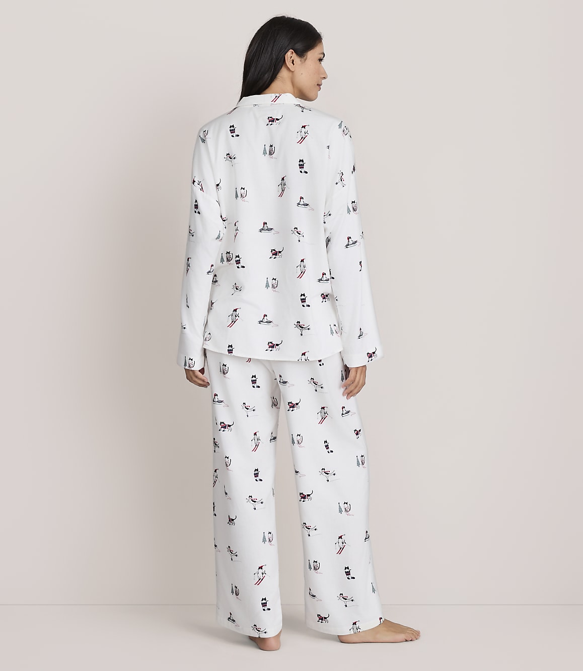 A woman stands with her back to the camera wearing white patterned pajamas against a plain, light-colored background.