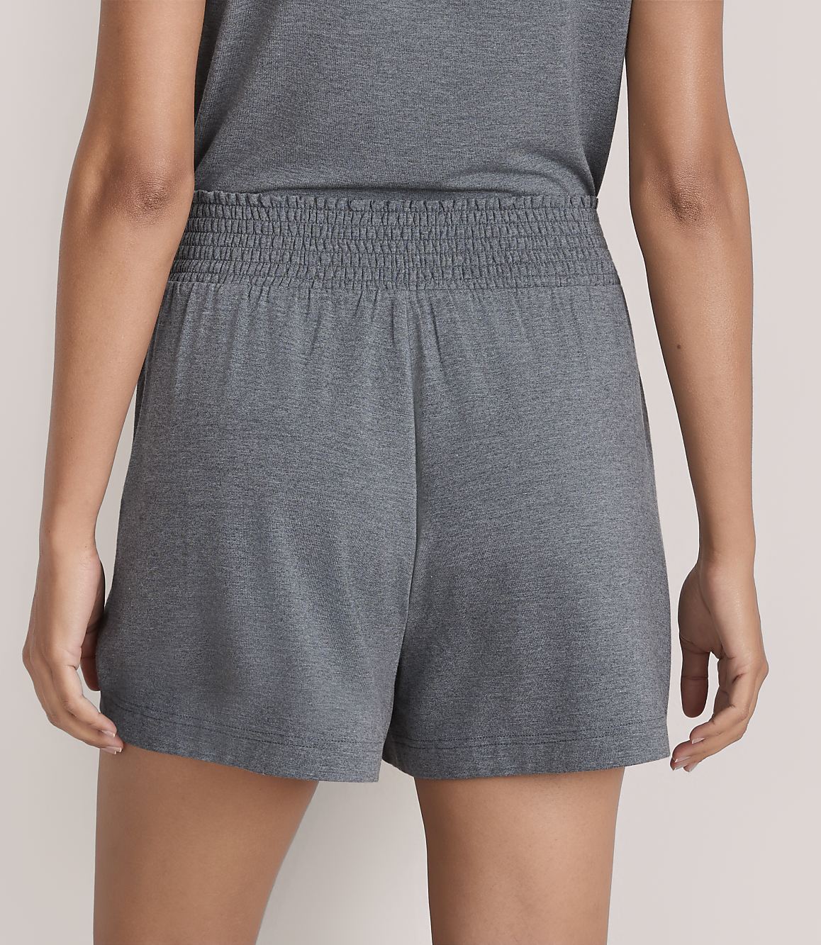A person wears grey shorts and a matching top against a plain, light-colored background.