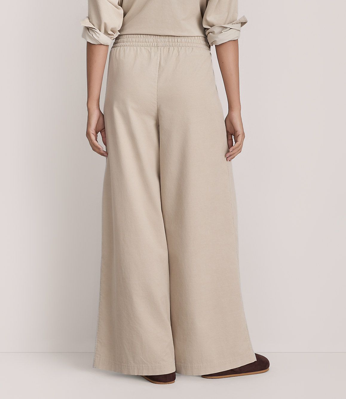 A person wearing wide-leg beige trousers and a matching top stands against a plain, light-colored background.