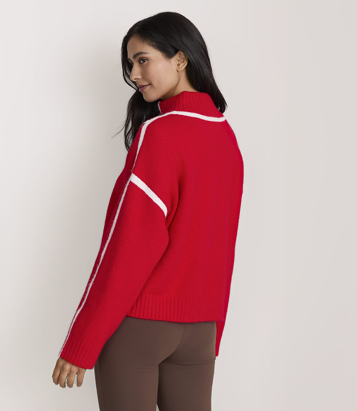 A woman wearing a red sweater and brown leggings stands against a plain white background.