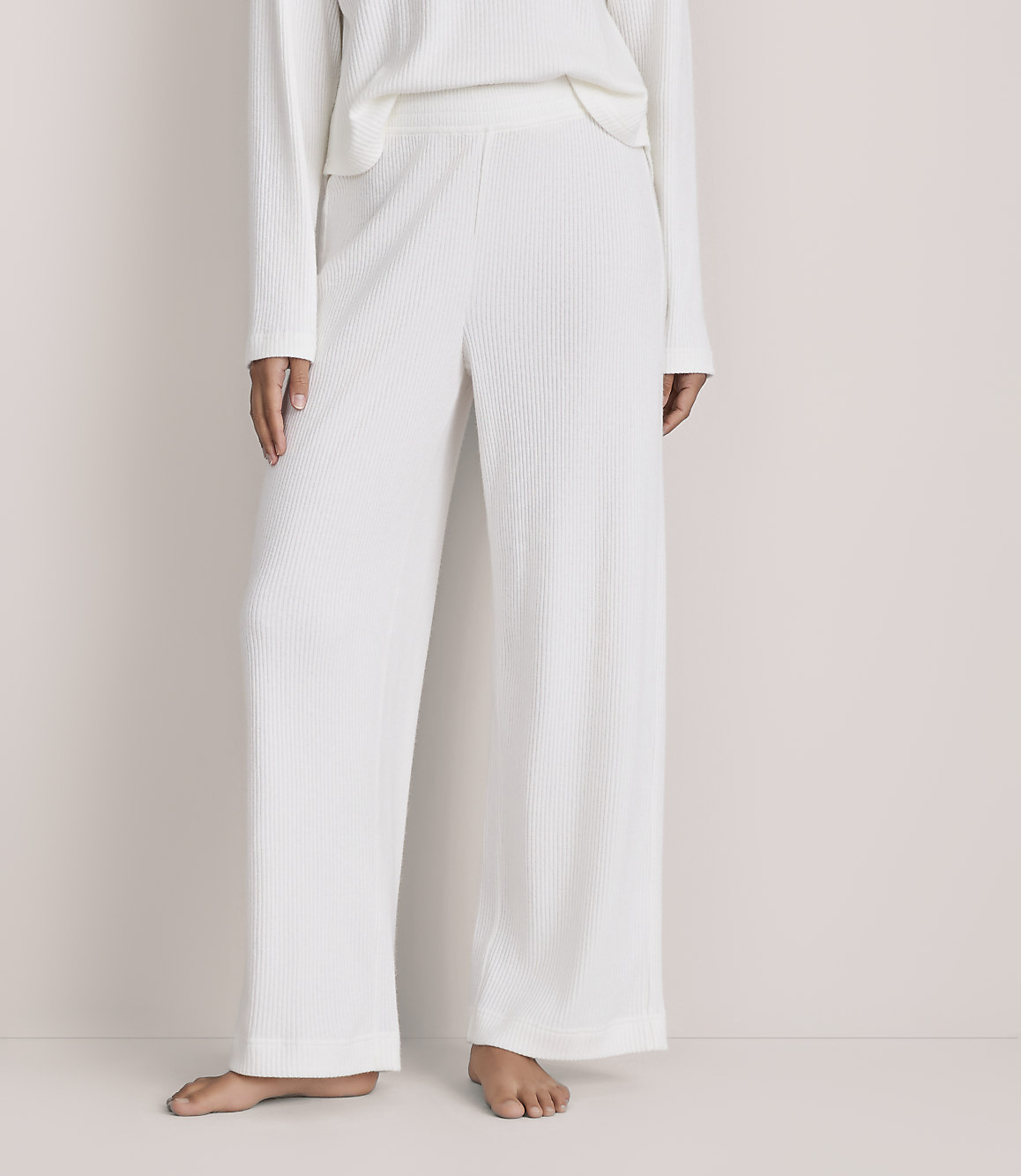 A person wearing a white ribbed knit matching set stands barefoot against a plain, light-colored background.