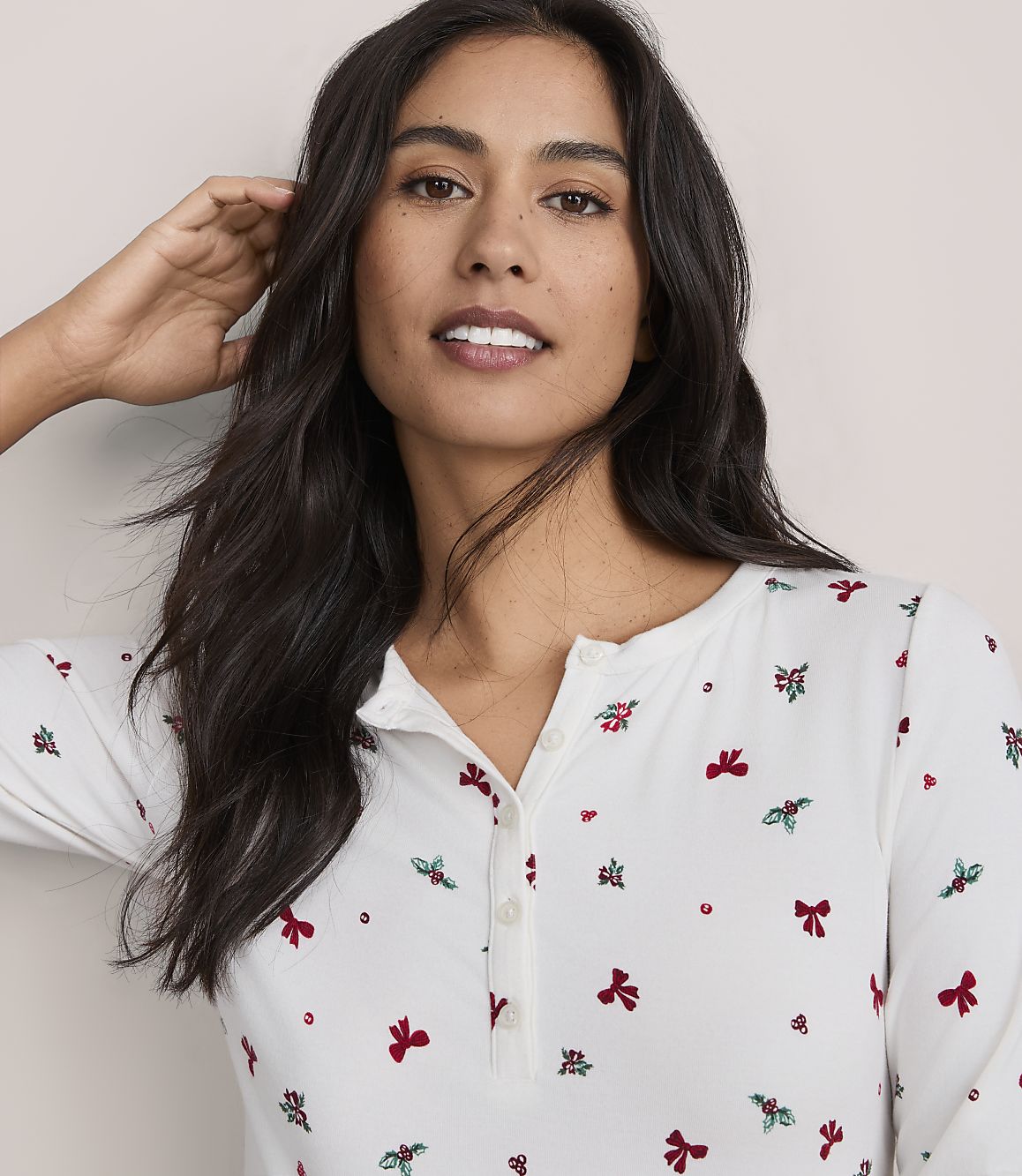 A woman with long dark hair wearing a white floral print shirt poses against a plain light-colored background.