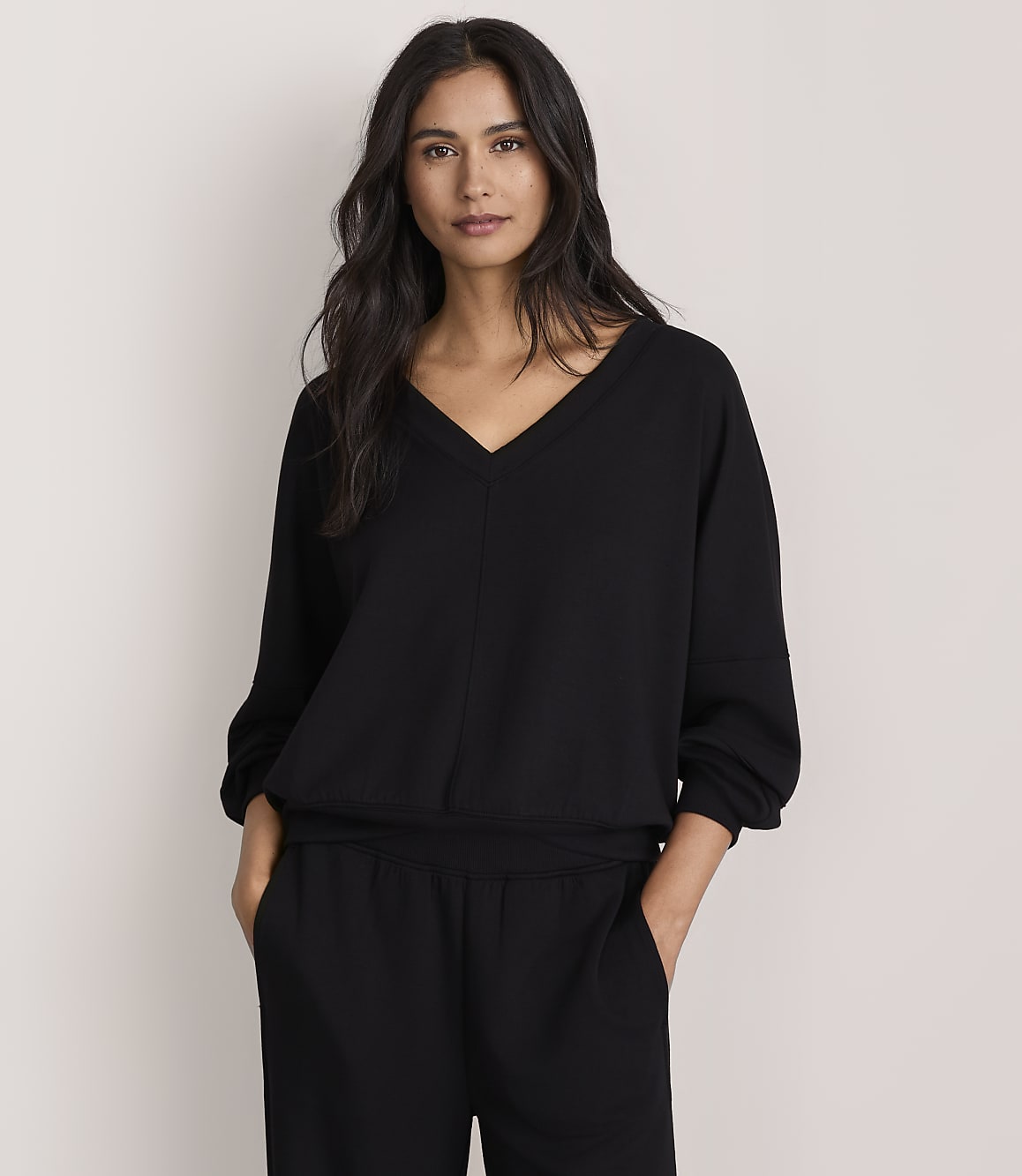 A woman wearing a black v-neck top and matching pants stands against a plain, light-colored background.