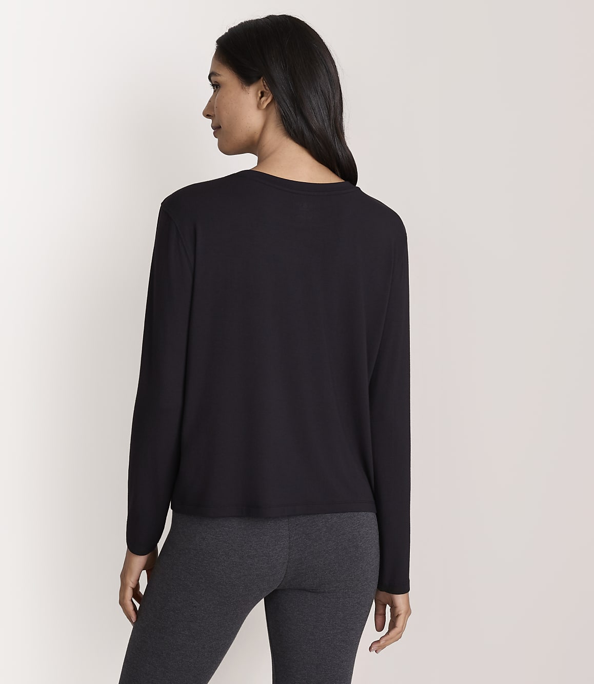 A woman wearing a black long-sleeved shirt and dark grey leggings stands against a plain white background.