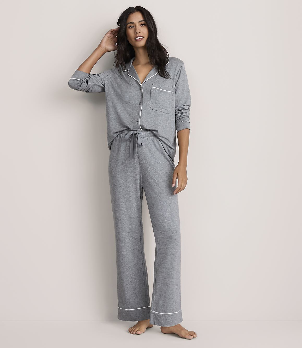 A woman wearing grey pajamas with white piping stands against a plain, light-colored background.