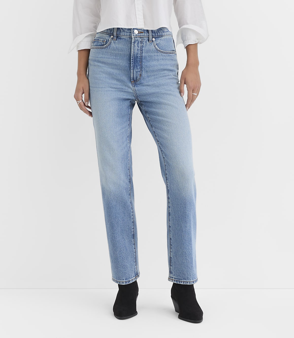 A person wearing light-wash denim jeans and black ankle boots stands against a plain white background.