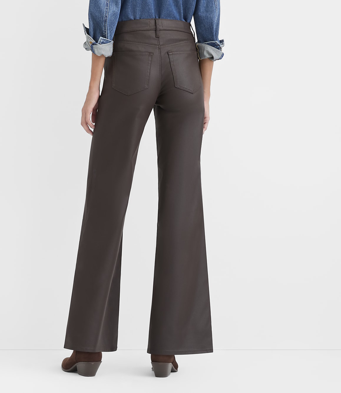 A person wearing a blue denim shirt and brown wide-leg trousers stands against a plain white background.