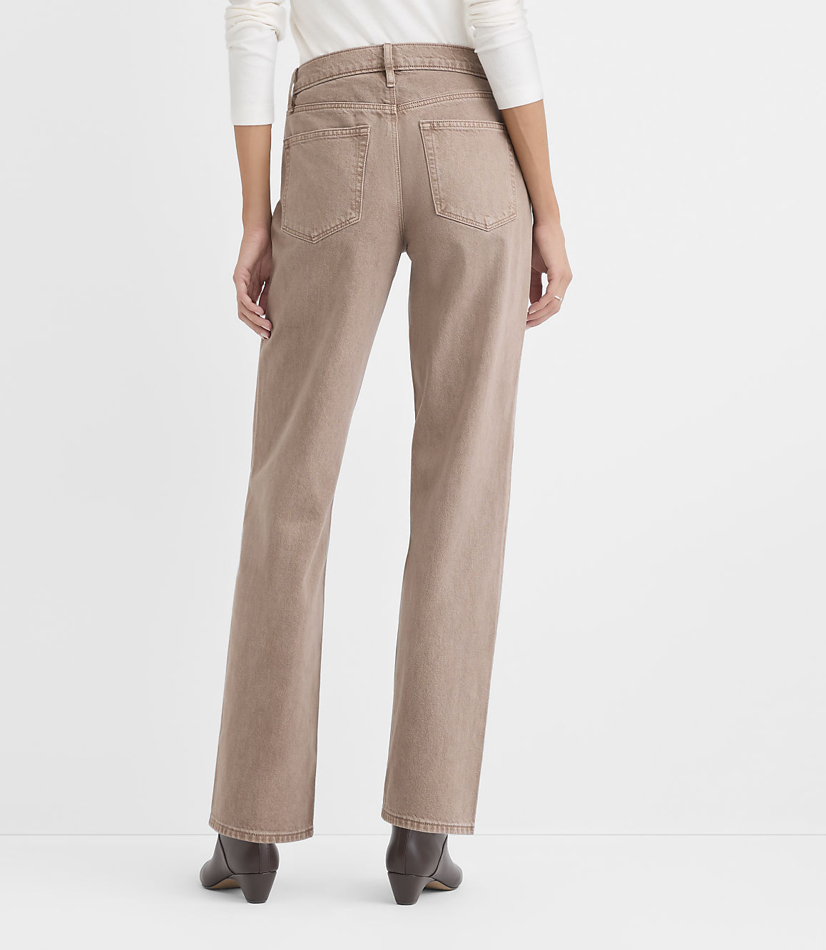 A person wearing a white top, tan straight-leg jeans, and dark brown boots stands against a plain white background.