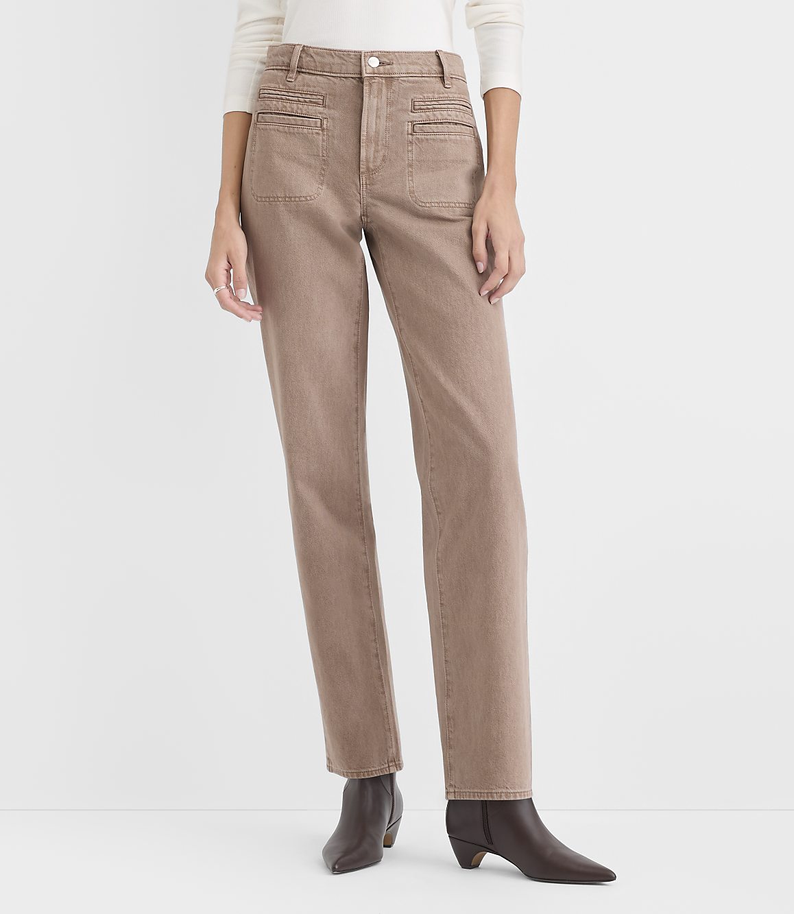 A person wearing a white top, tan trousers, and brown boots stands against a plain white background.