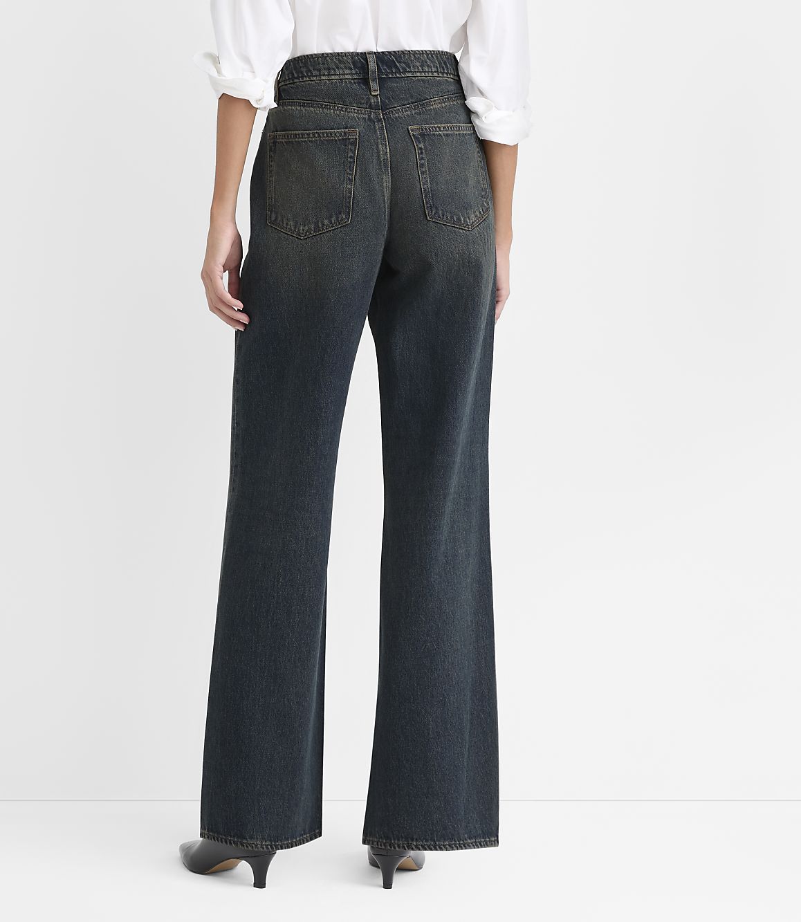A person wearing a white shirt and wide-leg dark blue jeans stands against a plain white background.