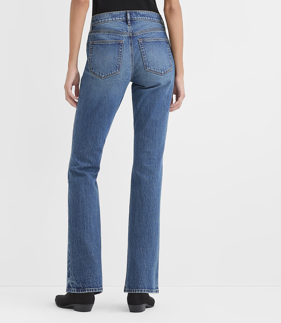 A person wearing blue jeans and black shoes stands against a plain white background.