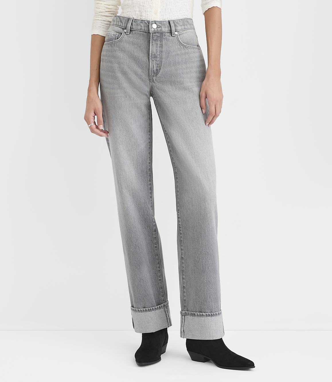 A person wears grey cuffed jeans and black ankle boots against a plain white background.