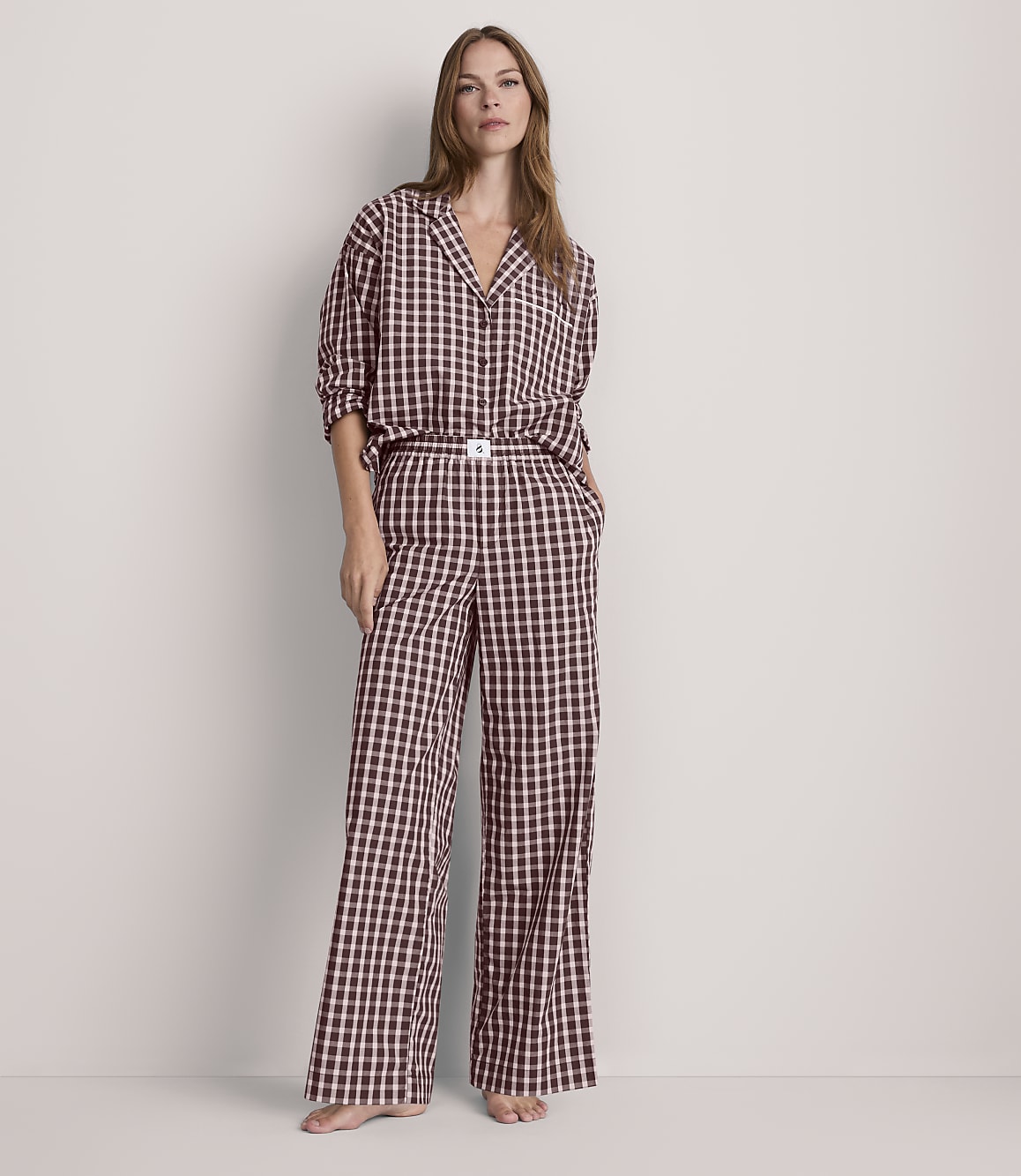 A woman stands in a light-colored room wearing a black and white checkered pajama set, with her hands in her pockets.