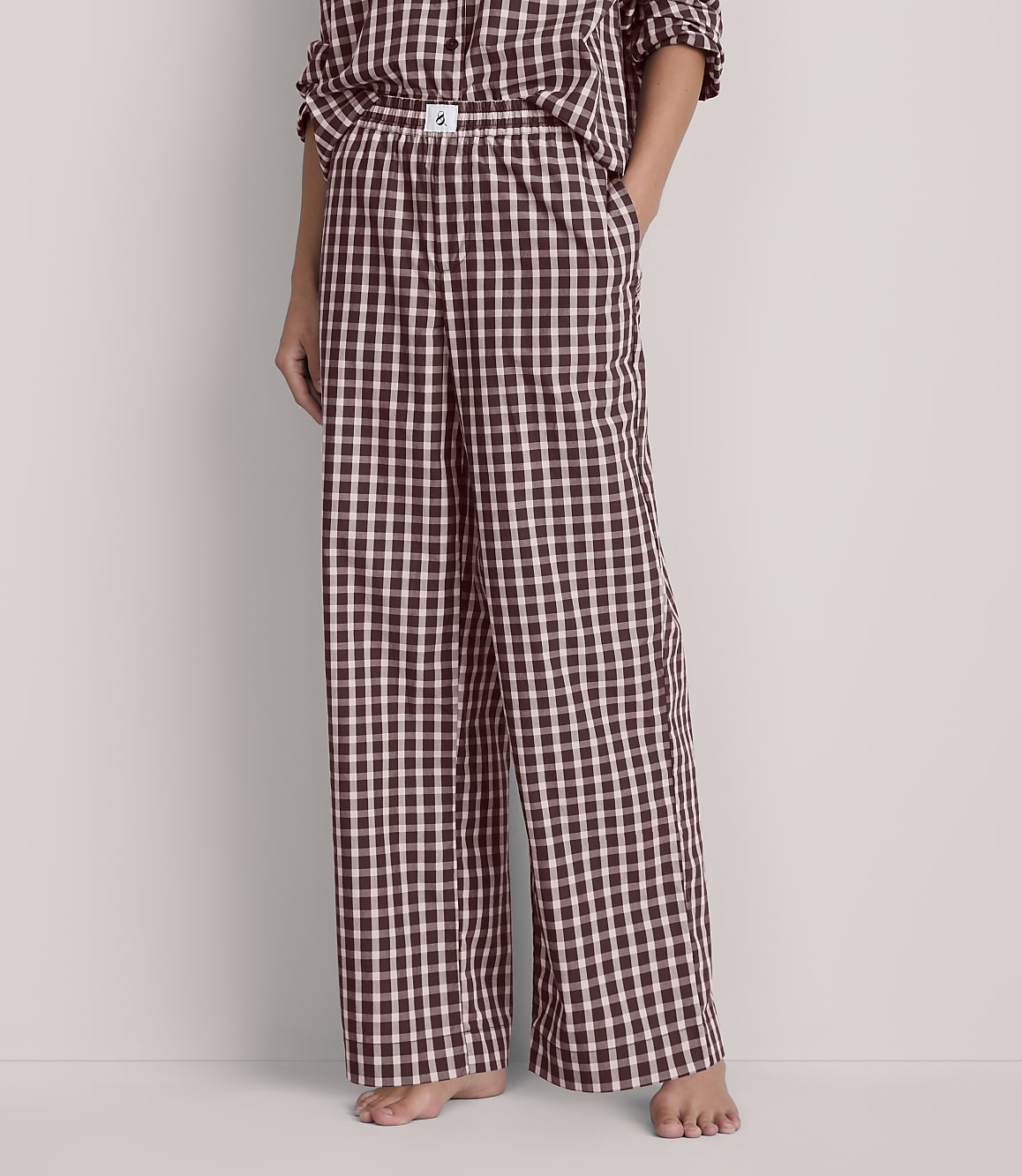A person stands in wide-leg, black and white checkered pajama pants in the foreground, against a plain, light-colored background.