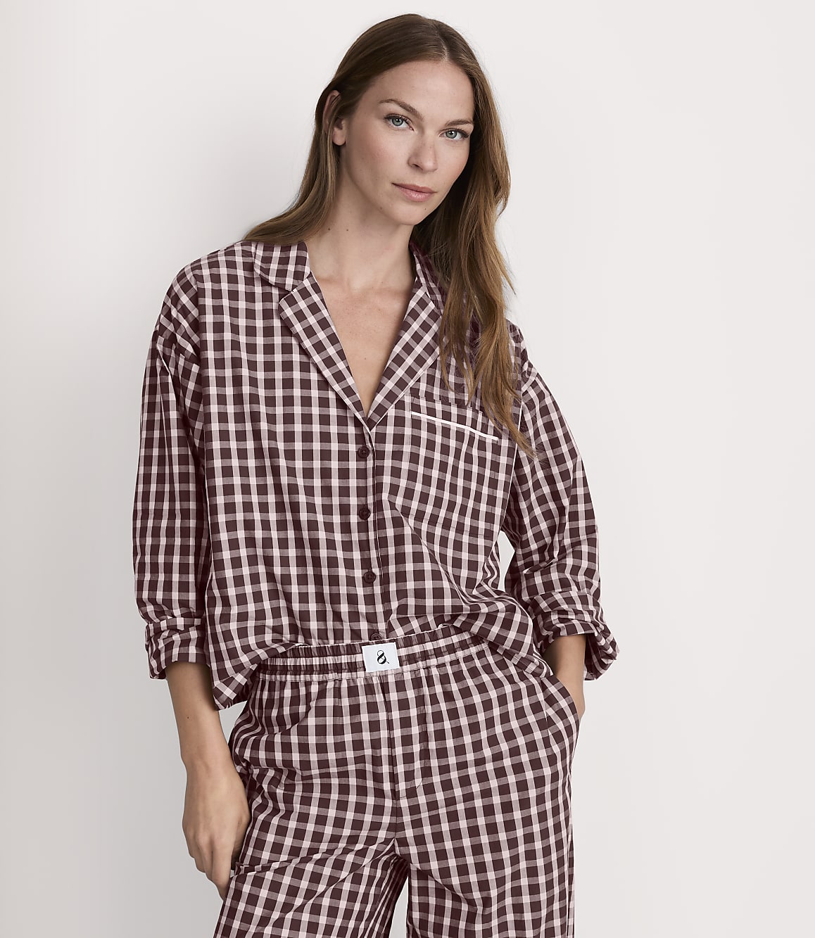 A woman in brown and white checkered pajamas stands against a plain white background.