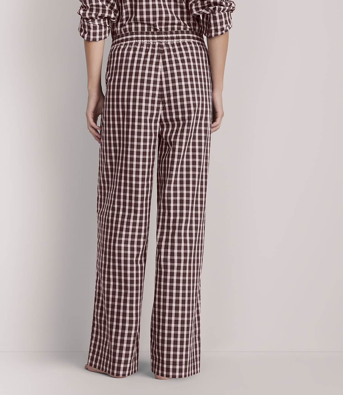 A person wearing black and white checkered pajama pants stands against a plain, light-colored background.