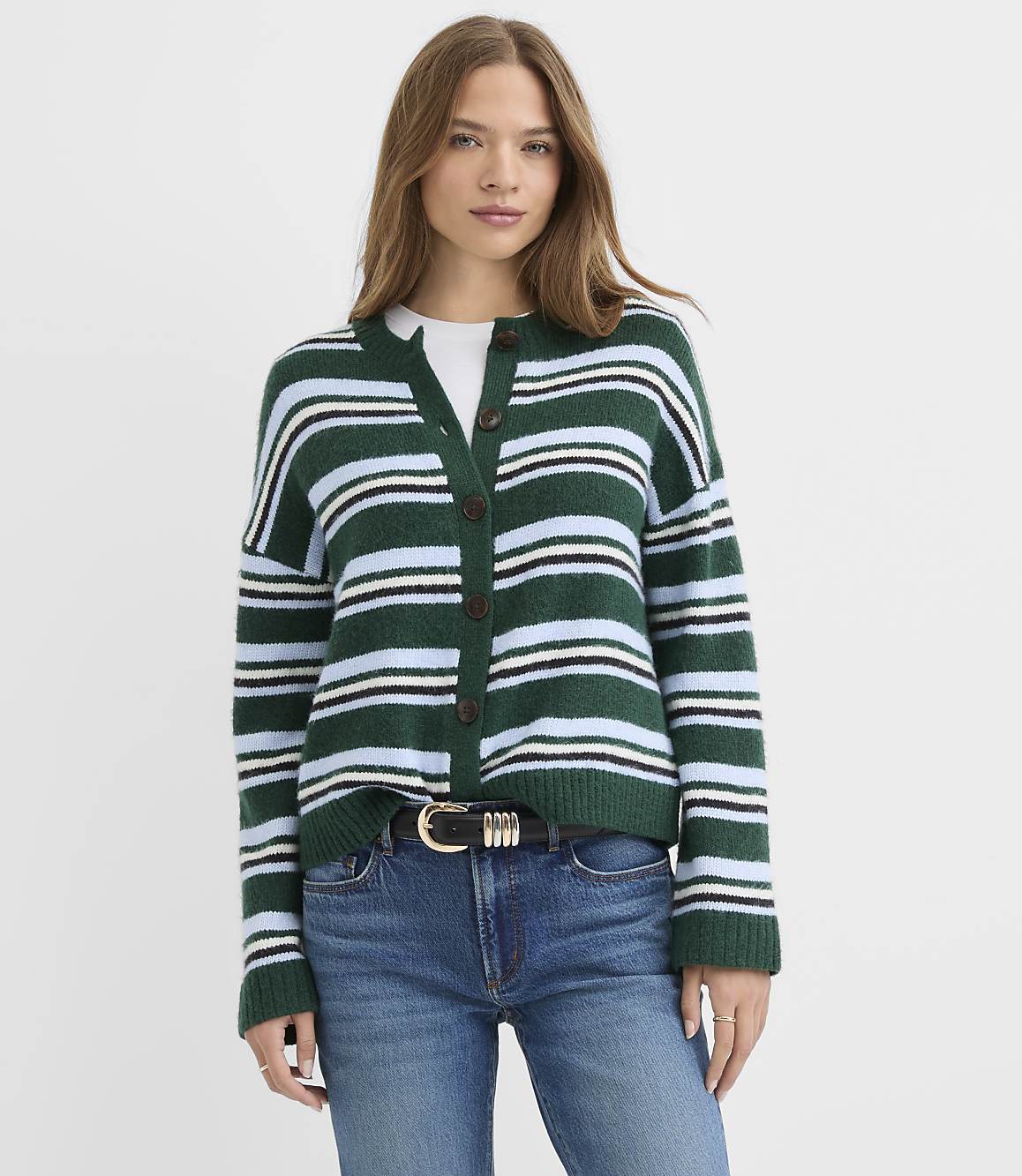 A woman wearing a green and blue striped cardigan and blue jeans stands against a plain white background.