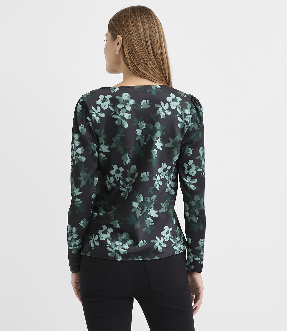 A woman wearing a black floral print blouse and black pants stands with her back to the camera against a plain white background.