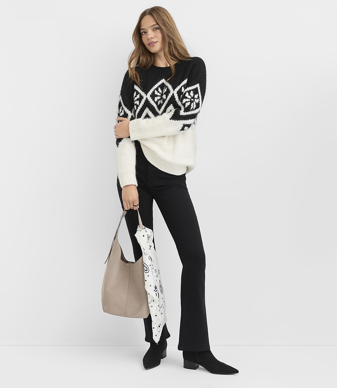 A woman wearing a black and white patterned sweater and black pants stands against a plain white background.