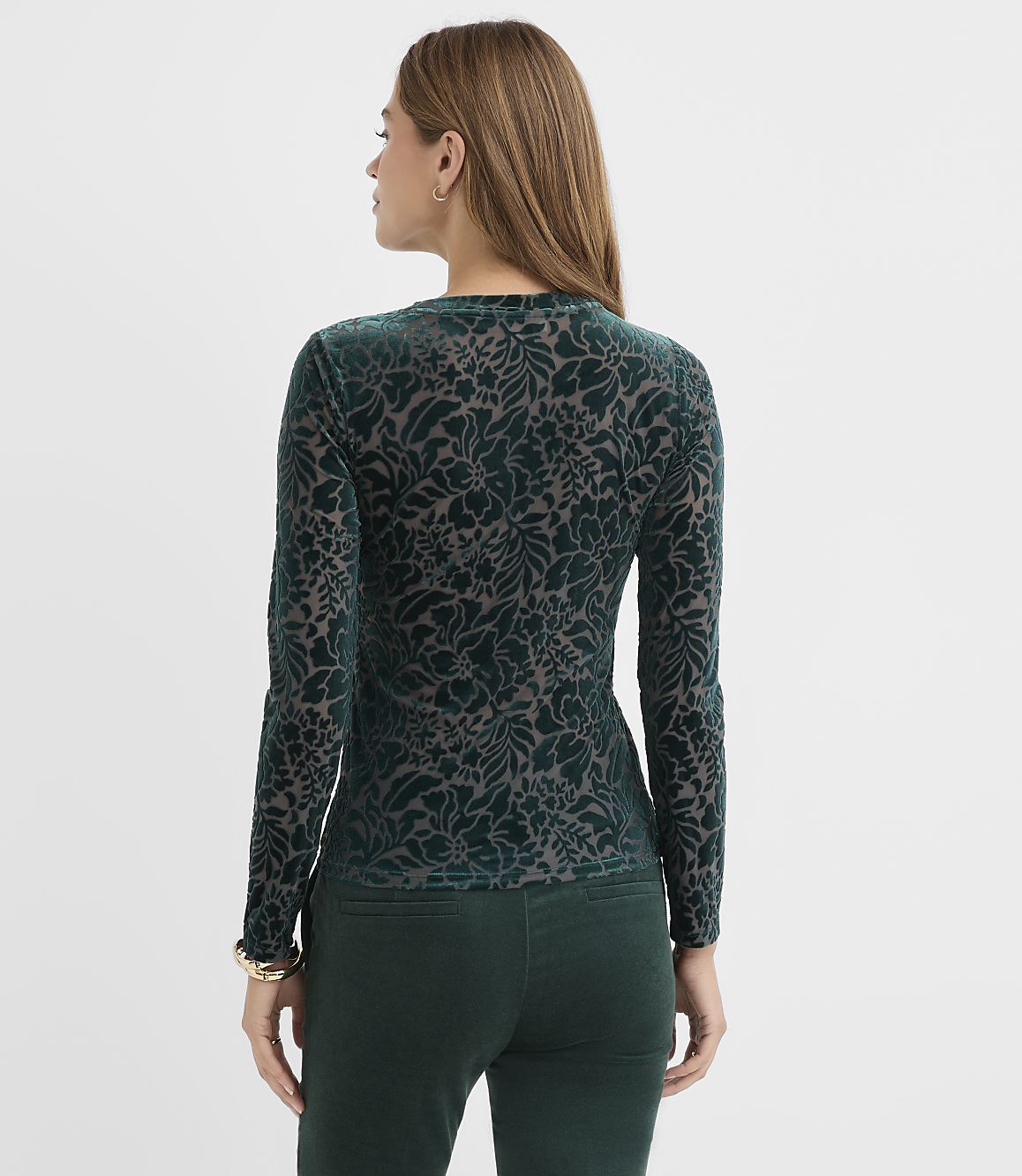 A woman wearing a green floral velvet top and matching pants stands against a plain white background.